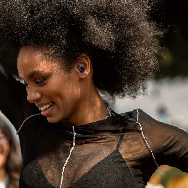 Woman enjoying music outdoors while wearing a blue earplug
